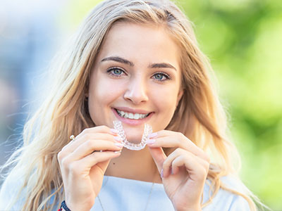A young woman with straight white teeth is smiling at the camera while holding a toothbrush.