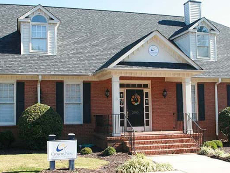 The image shows a two-story residential building with a brick facade, a front porch with columns, and a sign indicating 123 Main Street.