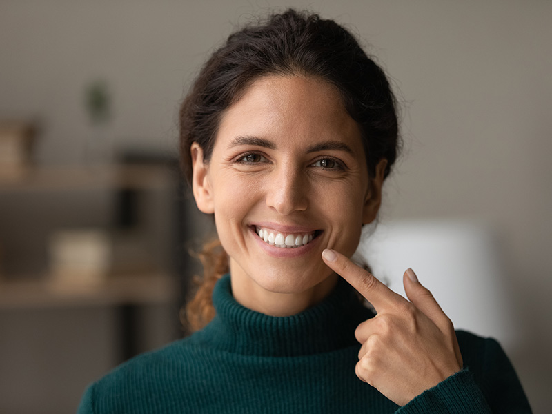 A smiling woman with dark hair, wearing a blue top and a ring on her finger, posing for the camera.