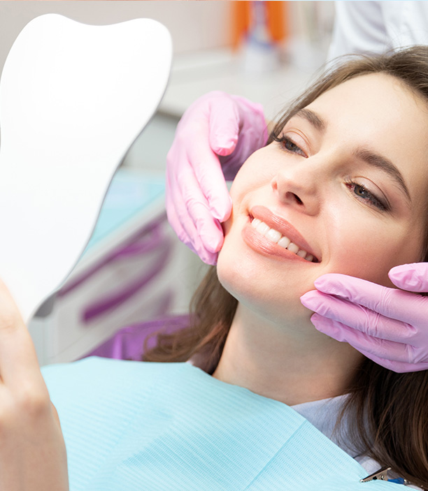 This is an image of a dental care setting where a woman is seated in a dentist s chair, receiving treatment, with a dental mirror and a professional attendant assisting her.